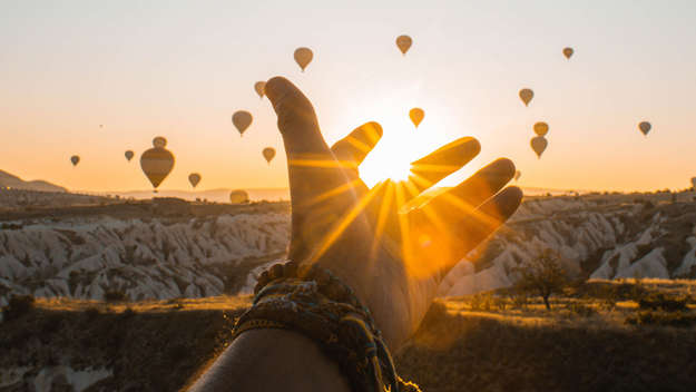 Hand im Sonnenaufgang mit Heißluftballons im Hintergrund