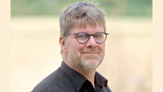 Zu sehen ist Pfarrer Dr. Fabian Vogt im Portrait. Er trägt hellbraune kurze Haare und eine dunkle runde Brille. Er hat einen Dreitagebart und trägt ein schwarzes Hemd