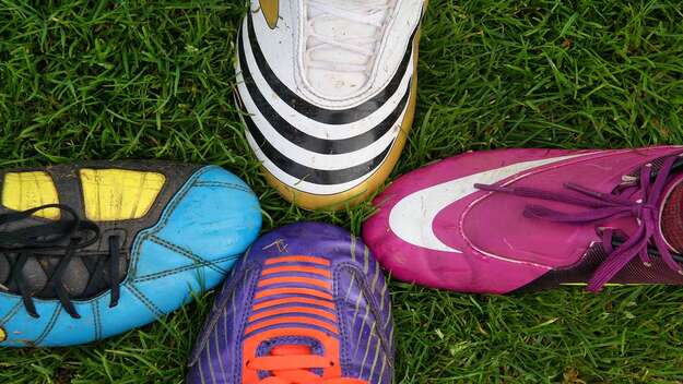 Vier verschiedene Fußballschuhe berühren sich Spitze an Spitze als Ausdruck für Teamwork und Zusammenhalt.