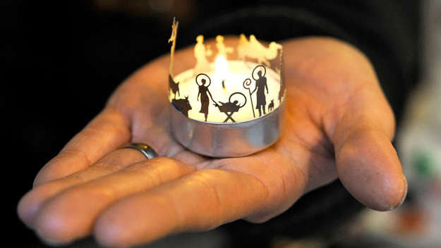 Eine Frau hält eine Minikrippe aus Edelstahl auf der Hand. Die Minikrippe wurde zwischen Wachs und Aluschale eines Teelichts angebracht.