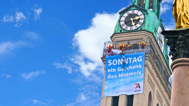 Aktivist*innen hängen ein Banner an Kirchturm auf.