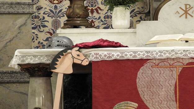 Ein Holzpferd lehnt am Altar einer Kirche. Ein Helm liegt ebenfalls darauf