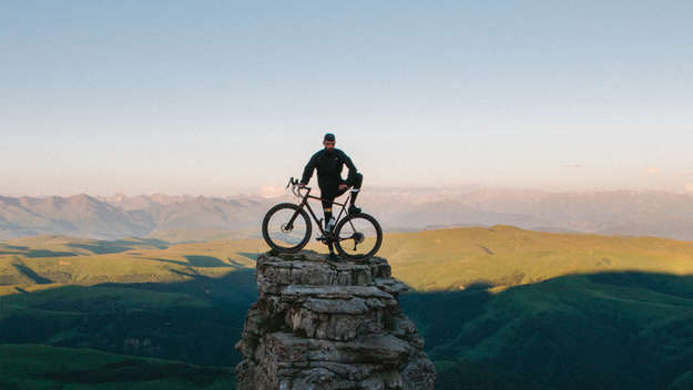Mann steht mit Fahrrad auf einem Berg