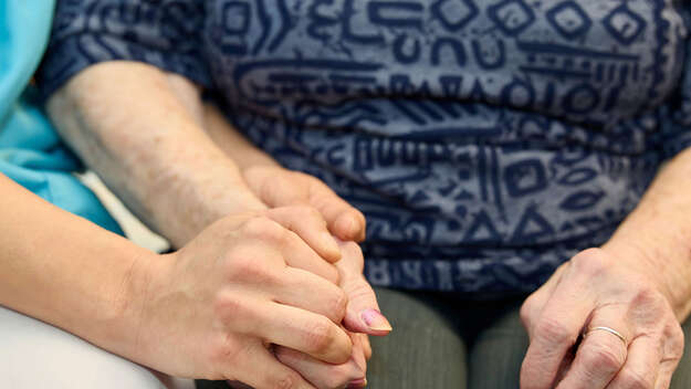 APHS: Pflegerin hält die Hand einer Bewohnerin