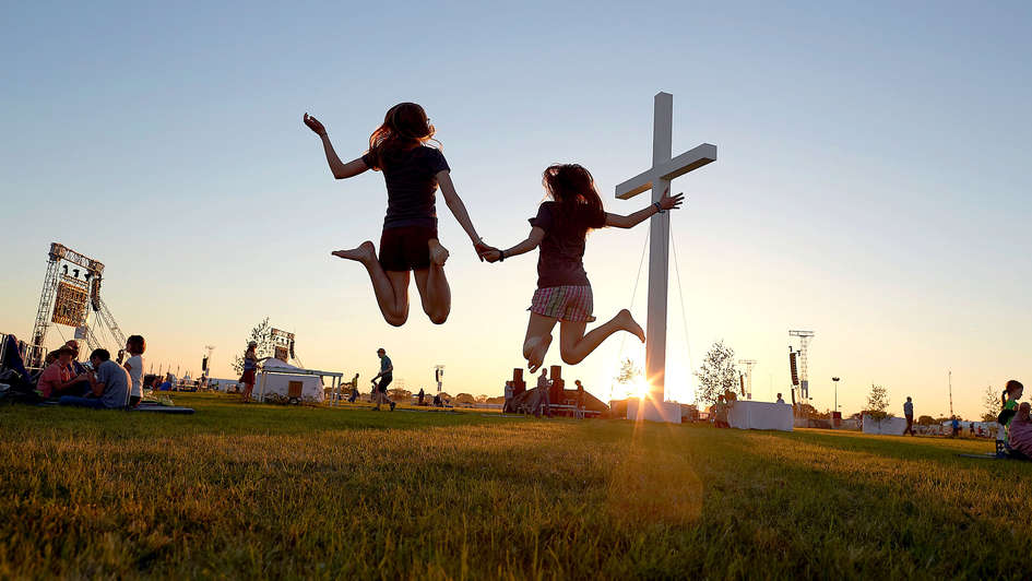 Zwei Mädchen springen vor einem Kreuz