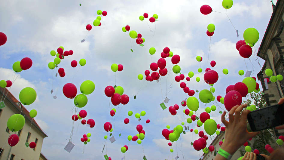 Rosane und grüne Luftballons fliegen in Richtung Himmel