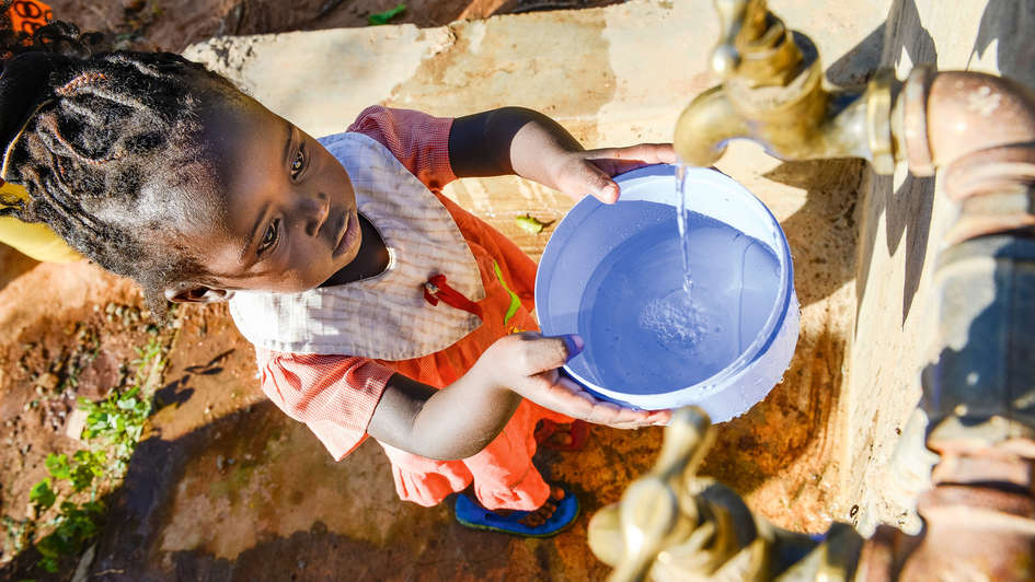 Mädchen hält einen Eimer unter einen Wasserhahn Mädchen hält einen Eimer unter einen Wasserhahn