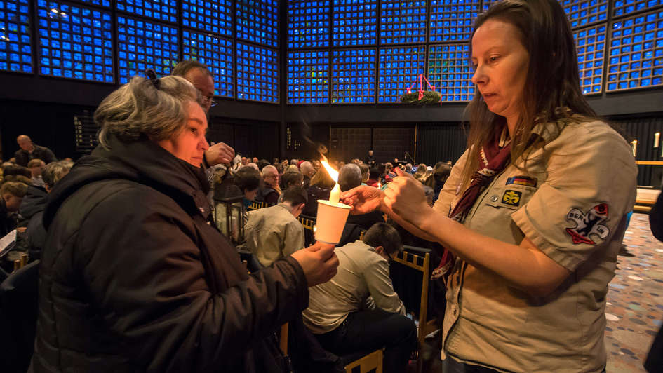 Pfadfinderin zündet Kerze einer Gottesdienstbesucherin an