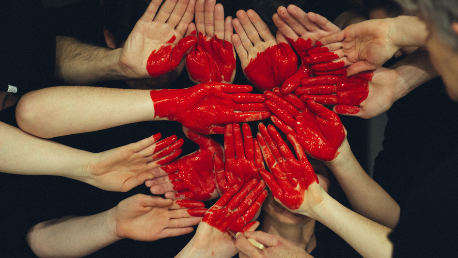Hände mehrerer Personen sind rot angemalt und ergeben ein Herz