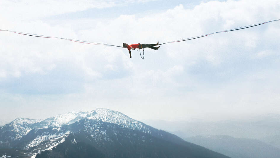 Ein Mann liegt in großer Höhe auf einer Slackline. Ein Mann liegt in großer Höhe auf einer Slackline.