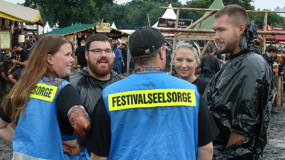 'Kadi', Pastorin Katharina Schunck, mit ihrem Festivalseelsorge-Kollegen Fabian Schmidt im Gespräch mit Wacken-Besucher*innen aus Speyer