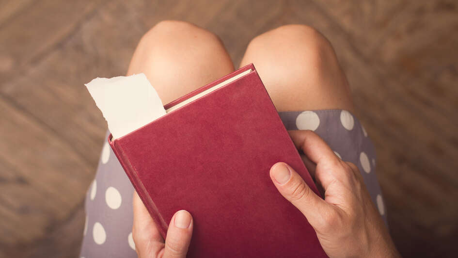 Frau hält ein Buch auf ihrem Schoß.