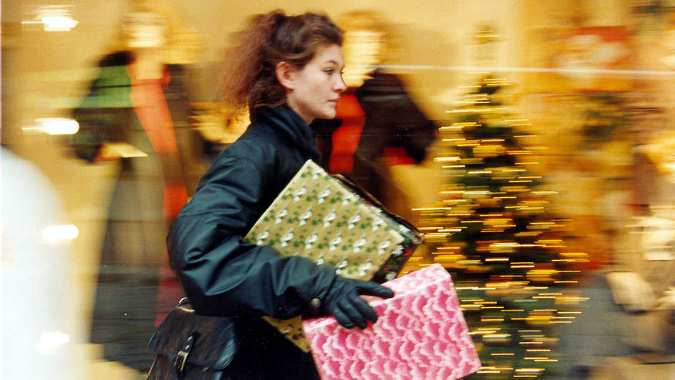 Eine  Frau mit Paketen unterm Arm eilt durch einen weihnachtlich geschmückten Laden