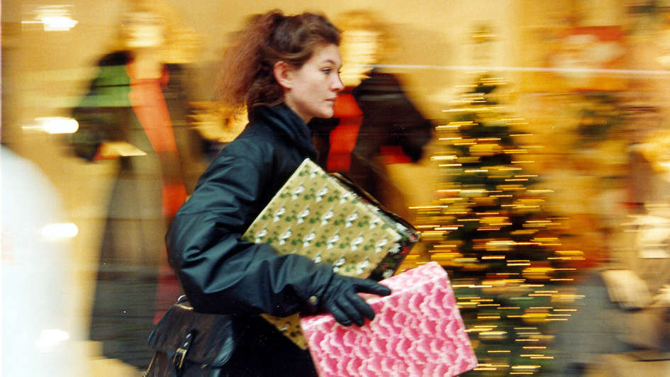 Eine Frau mit Paketen unterm Arm eilt durch einen weihnachtlich geschmückten Laden Eine Frau mit Paketen unterm Arm eilt durch einen weihnachtlich geschmückten Laden