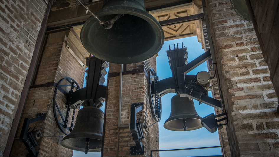 Glockenstuhl eines Kirchturms mit drei Glocken vor blauem Himmel