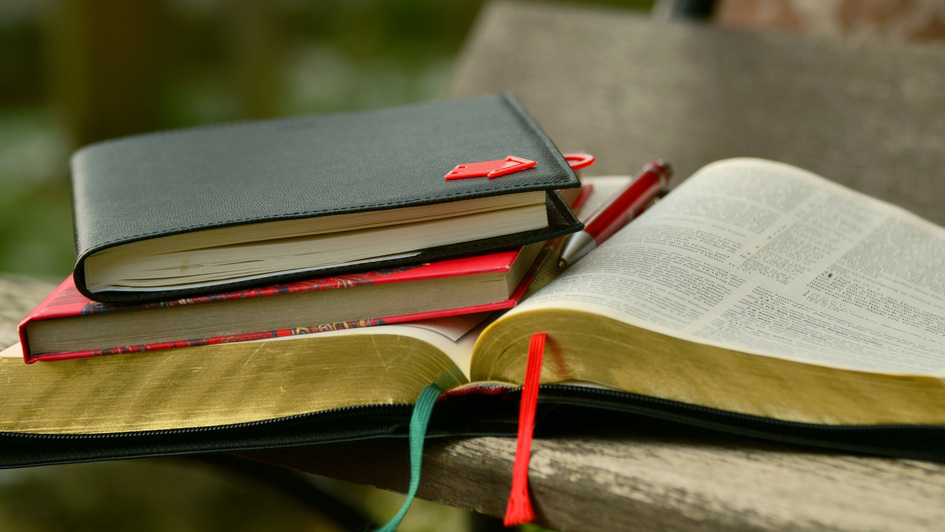 Eine aufgeschlagene Bibel und weitere Bücher liegen gestapelt Eine aufgeschlagene Bibel und weitere Bücher liegen gestapelt