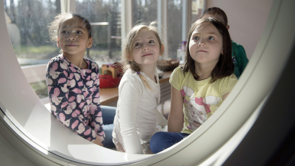 Drei Kinder im evangelischen Kindergarten 'Brummkreisel' im westfaelischen Espelkamp schauen durch ein rundes Fenster