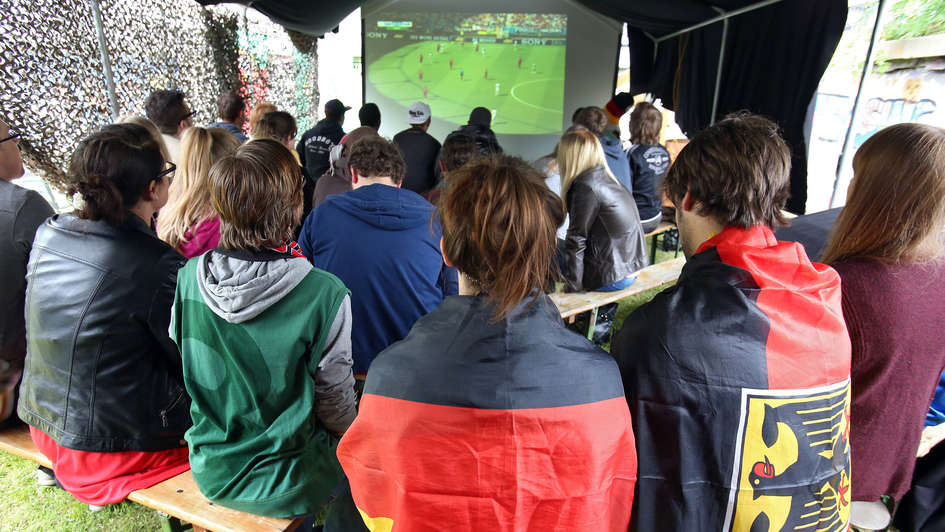 Public Viewing unter freiem Himmel im evangelischen Weigle-Haus in Essen: Fans sitzen, teils in Deutschland-Fahnen gehüllt, vor einem Bildschirm