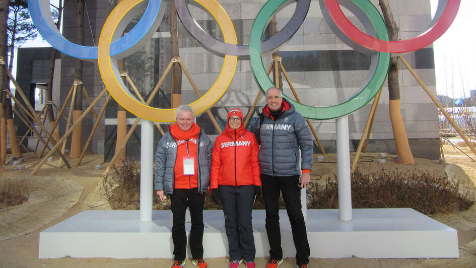 Die Olympiapfarrer Jürgen Hünten und Thomas Weber mit Christin Schwuchow, Mitarbeiterin des Deutschen Olympischen Sportbunds vor den olympischen Ringen Die Olympiapfarrer Jürgen Hünten und Thomas Weber mit Christin Schwuchow, Mitarbeiterin des Deutschen Olympischen Sportbunds vor den olympischen Ringen