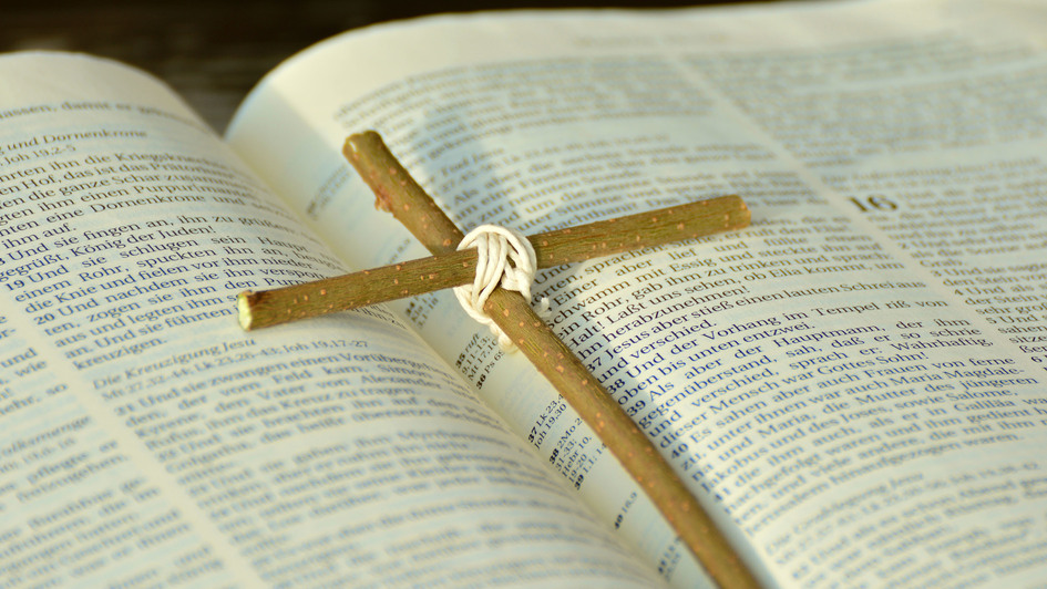 Ein Kreuz aus zwei Holzstäben liegt auf einer aufgeschlagenen Bibel