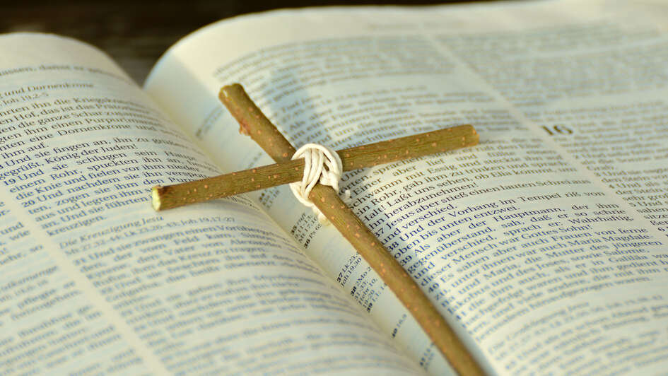 Ein Kreuz aus zwei Holzstäben liegt auf einer aufgeschlagenen Bibel Ein Kreuz aus zwei Holzstäben liegt auf einer aufgeschlagenen Bibel