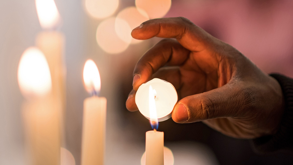 Eine Hand hält ein Teelicht an eine Kerzenflamme, um es anzuzünden. Eine Hand hält ein Teelicht an eine Kerzenflamme, um es anzuzünden.