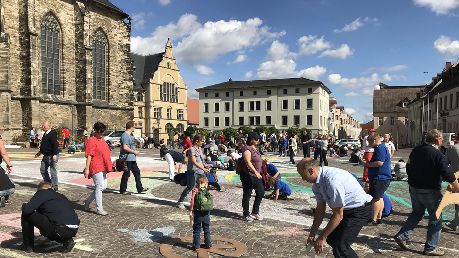Malaktion auf dem Marktplatz in Köthen: Lauter Menschen malen mit farbiger Kreide Symbole des Friedens aufs Pflaster
