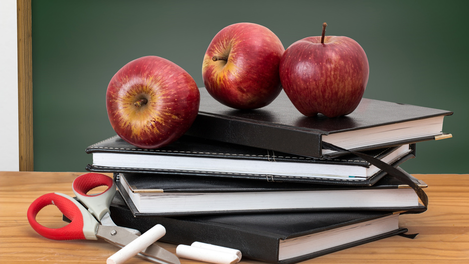 Bücher, Schere, Kreide und ein Apfel vor einer Tafel