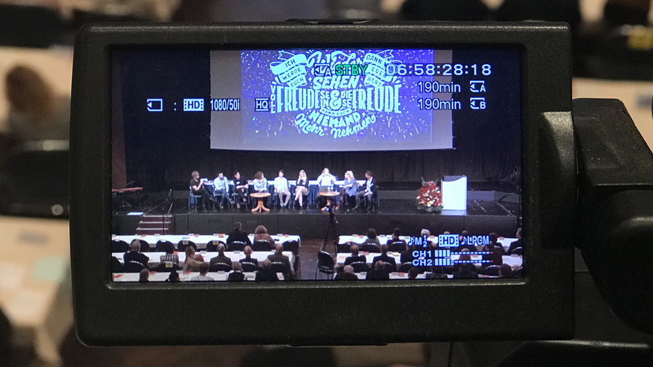 Kamera-Display mit jungen Menschen auf dem Podium der EKD-Synode im Bild