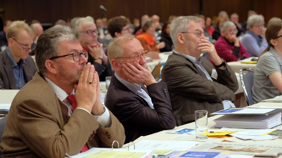 Zuhörer mit betroffenen Gesichtern im Plenum der EKD-Synode in Würzburg, während die Bischöfin Kirsten Fehrs den Bericht zur Verantwortung und Aufarbeitung sexualisierter Gewalt in der evangelischen Kirche vorträgt