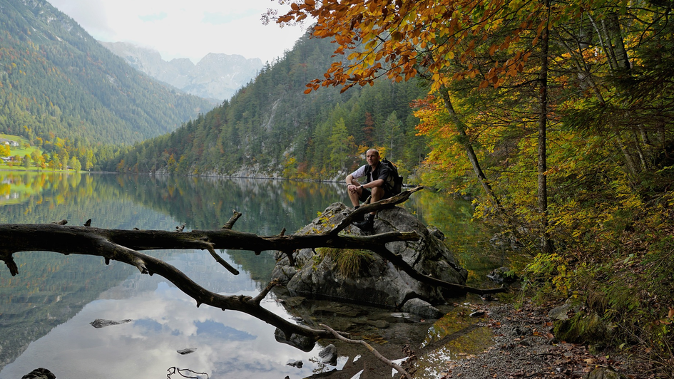 Mann sitzt am Seeufer vor Berglandschaft