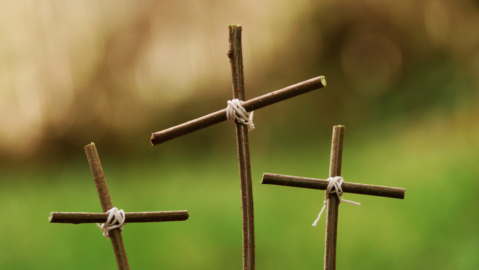 Drei Kreuze aus Ästen vor grünem Hintergrund