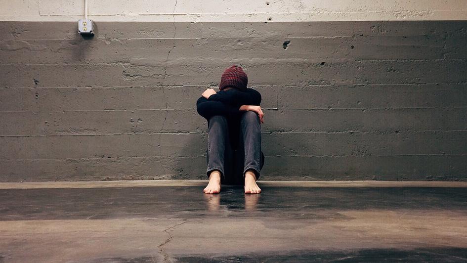 Ein Jugendlicher sitzt in einem kahlen Raum auf dem Fußboden, den Kopf auf die Arme gesenkt