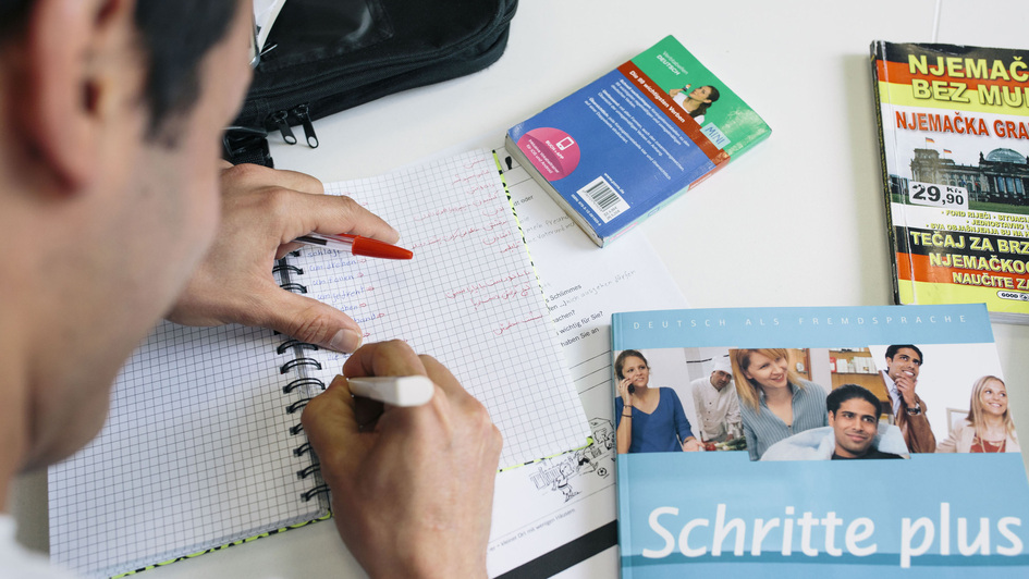 Blick über die Schulter eines Teilnehmers an einem Integrationskurs für Flüchtlinge. Vor ihm liegen Bücher, er schreibt in ein Heft