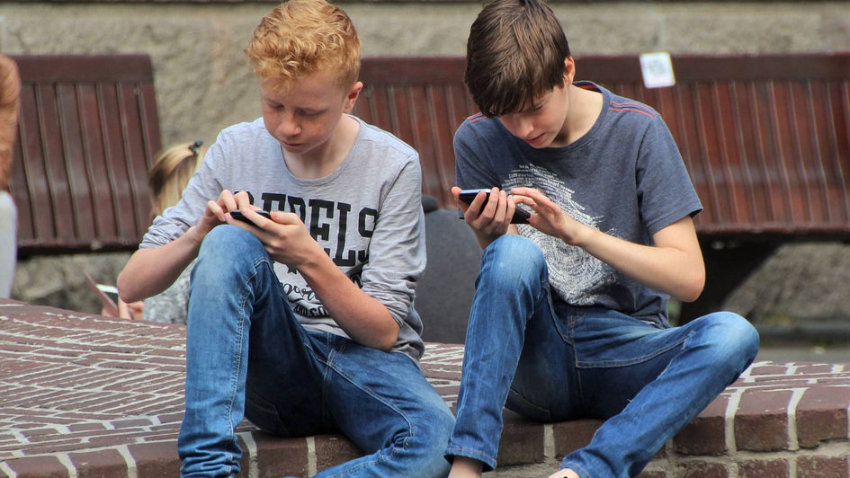 Zwei Jugendliche sitzen in ihre Smartphones vertieft nebeneinander Zwei Jugendliche sitzen in ihre Smartphones vertieft nebeneinander