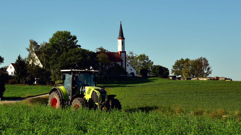 Traktor auf dem Feld, im Hintergrund ein Kirchturm
