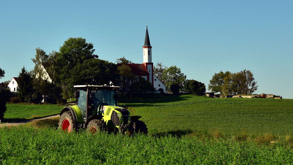 Traktor auf dem Feld, im Hintergrund ein Kirchturm Traktor auf dem Feld, im Hintergrund ein Kirchturm