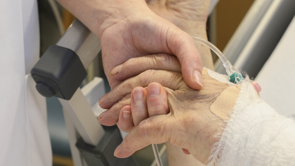Eine Krankenschwester hält auf einer Palliativstation die Hand eines Patienten