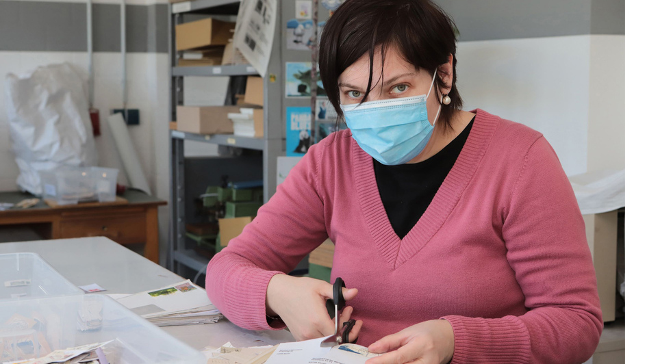 Beschäftigte mit Mundschutz in der Briefmarkenstelle der Bodelschinghschen Stiftung in Bielefeld schneidet Briefmarken aus. Beschäftigte mit Mundschutz in der Briefmarkenstelle der Bodelschinghschen Stiftung in Bielefeld schneidet Briefmarken aus.