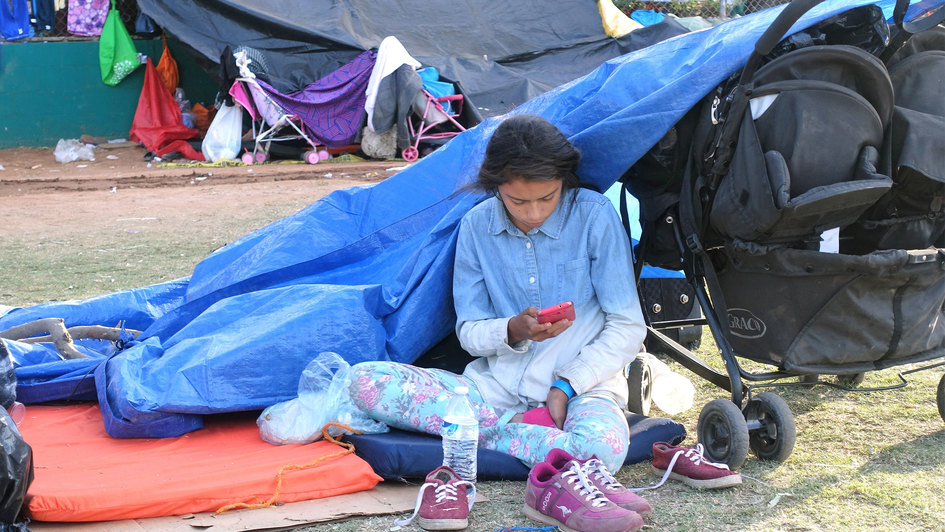 Junge Frau in einem Flüchtlingslager mit Kinderwagen sitzt unter einer Plane.