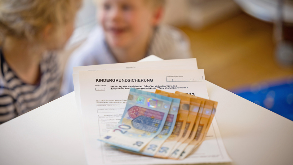 Formular Kindergrundsicherung mit Geldscheinen darauf und Kinder im Hintergrund