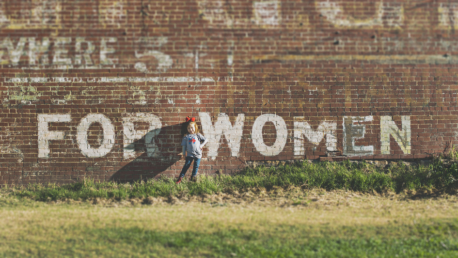 Schriftzug „For Women“ auf einer Wand und ein kleines Mädchen Schriftzug „For Women“ auf einer Wand und ein kleines Mädchen