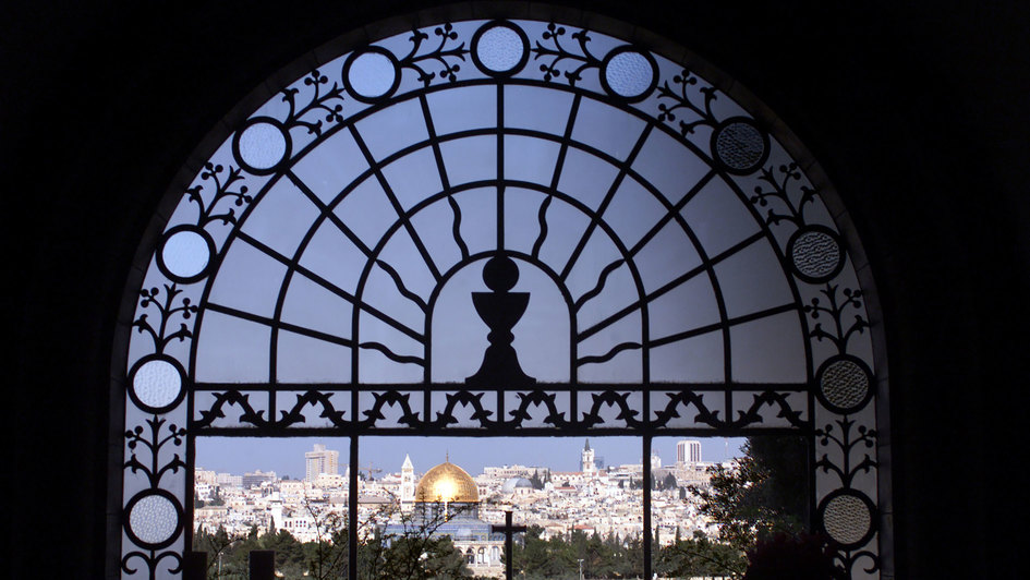 Blick auf Jerusalem durch das Fenster der Kirche 'Dominus Flevit'. Das Altarkreuz weist auf die Grabeskirche (mit zwei Kuppeln), links daneben der Felsendom und der Kirchturm der evangelischen Erlöserkirche.