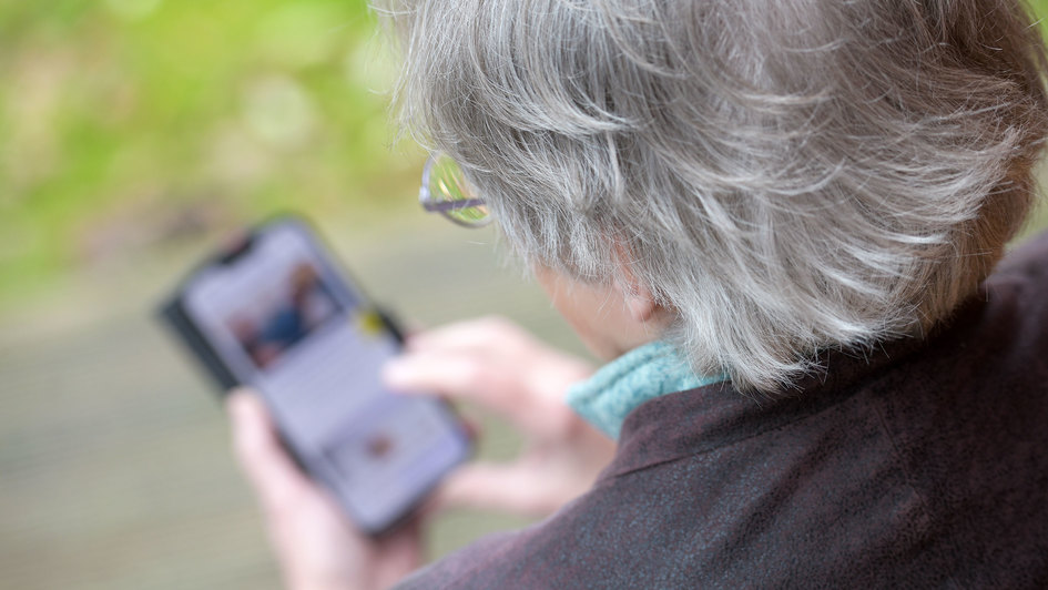 Themenbild Digitale Teilhabe älterer Menschen: Grauhaarige Frau mit Handy