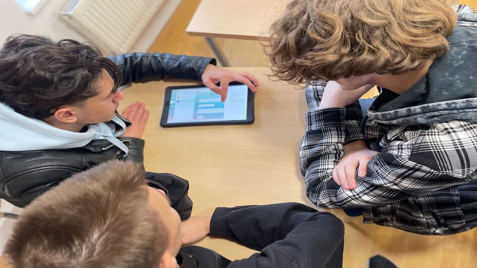 Drei Jugendliche spielen gemeinsam das Serious Game „Mission Ganymed“ an einem Tablet.