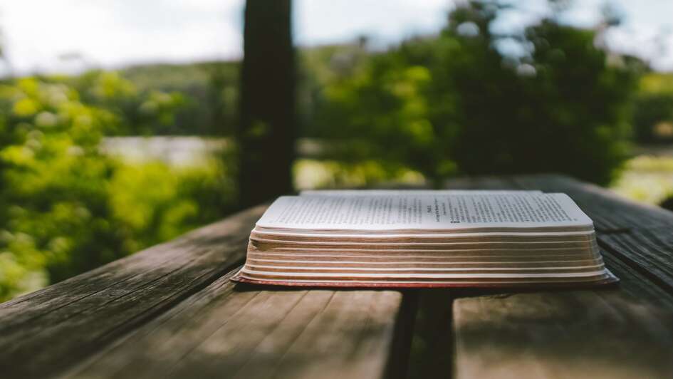 Aufgeschlagene Bibel auf einem Tisch im Freien Aufgeschlagene Bibel auf einem Tisch im Freien