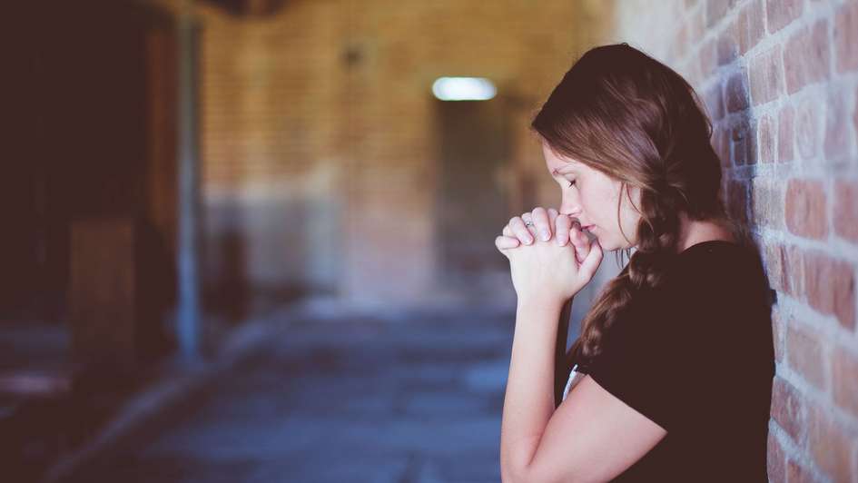 Eine junge Frau lehnt an einer Wand und betet