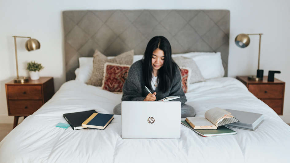 Eine junge Frau sitzt auf dem Bett und arbeitet am Laptop Eine junge Frau sitzt auf dem Bett und arbeitet am Laptop