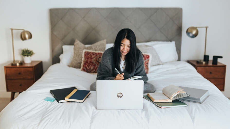Eine junge Frau sitzt auf dem Bett und arbeitet am Laptop Eine junge Frau sitzt auf dem Bett und arbeitet am Laptop