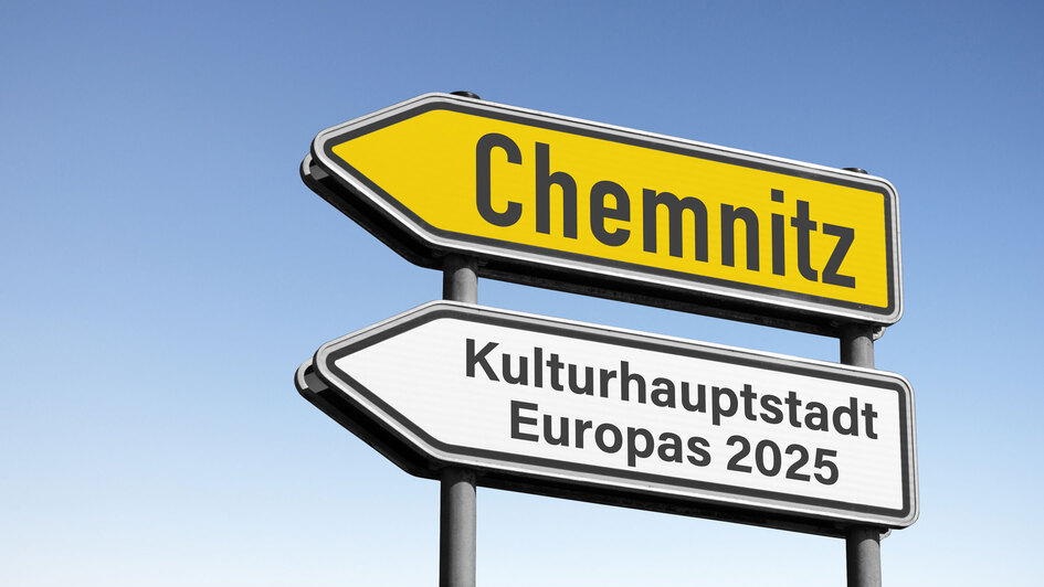Zwei Straßenschilder vor blauem Himmel: Das obere gelb mit der Aufschrift ‚Chemnitz‘, das untere weiß mit der Aufschrift ‚Kulturhauptstadt Europas 2025